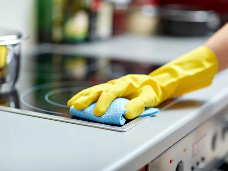 Close up of hand in Yellow glove cleaning electric stove top