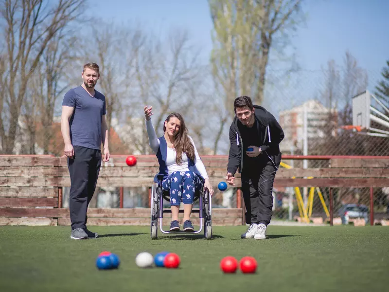 Disabled woman in wheelchair playing lawn bowls with two friends